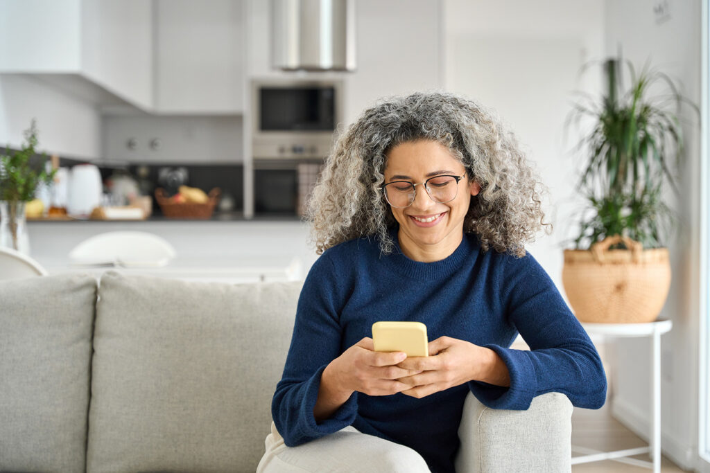 Kvinde sidder i en sofa med en telefon og smiler