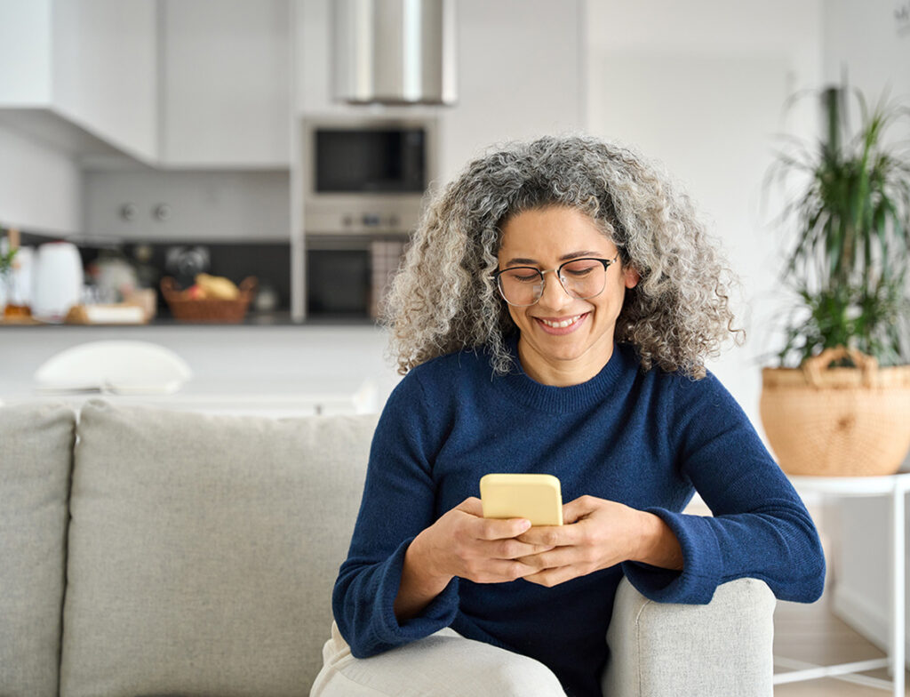 Kvinde sidder i en sofa med en telefon og smiler